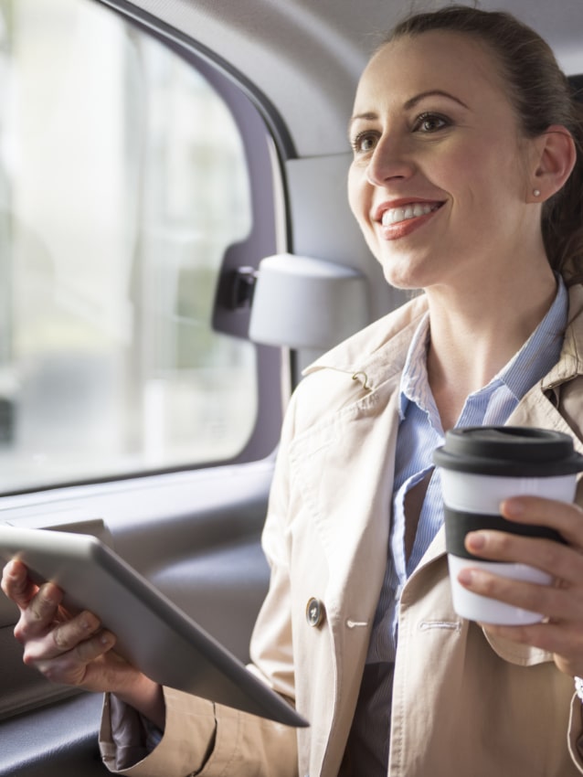 Nainen kahveineen taksin takapenkillä
